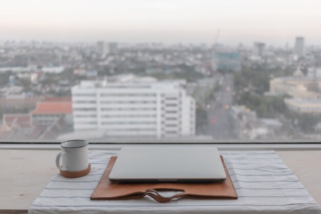 집에서 일하는 도시 전망 개념이 있는 노트북 및 흰색 커피 컵