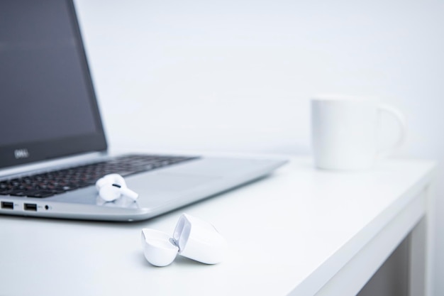 Cuffie senza fili della tazza bianca del computer portatile su un tavolo bianco luogo di lavoro