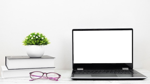 Laptop white screen with glasses and book on the desk workspace at home