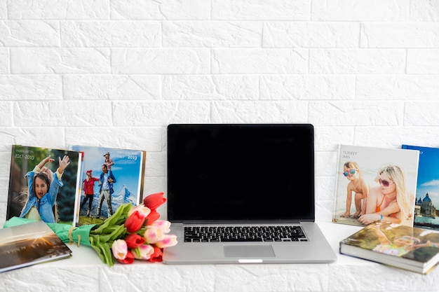 Laptop on white shelf with flowers. tulips, photo book.