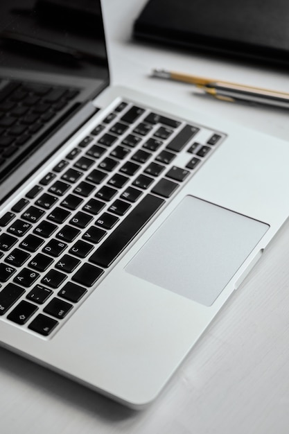 A laptop on a white table next to a notebook and pens.