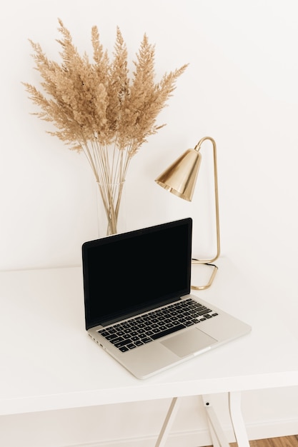 Photo laptop on white table with golden lamp and pampas grass