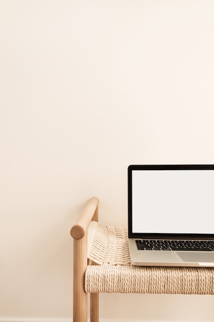 Laptop on wicker bench against white wall