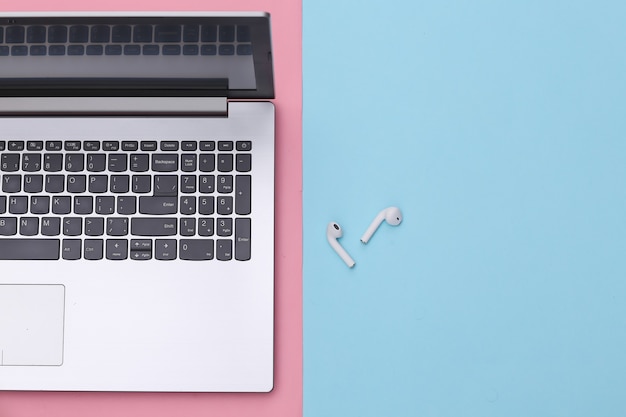 Laptop and wireless headphones on pink blue background. Top view