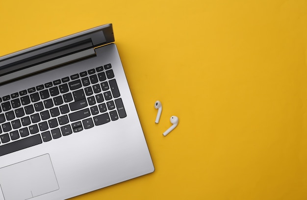 Laptop and wireless headphones on a yellow background. Top view