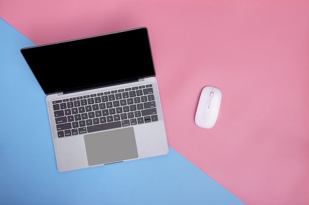 Laptop and wireless mouse on pink and blue background. copy space. top view.