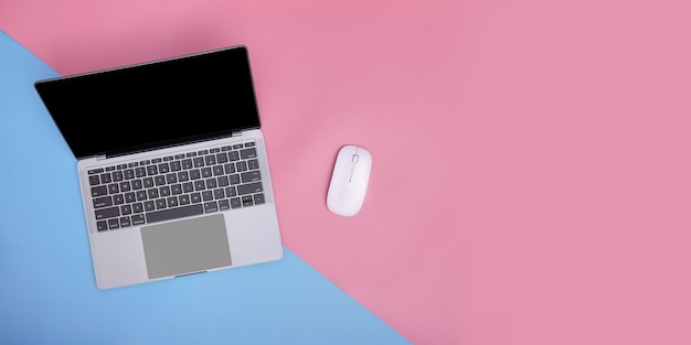 Laptop and wireless mouse on pink and blue background copy space top view