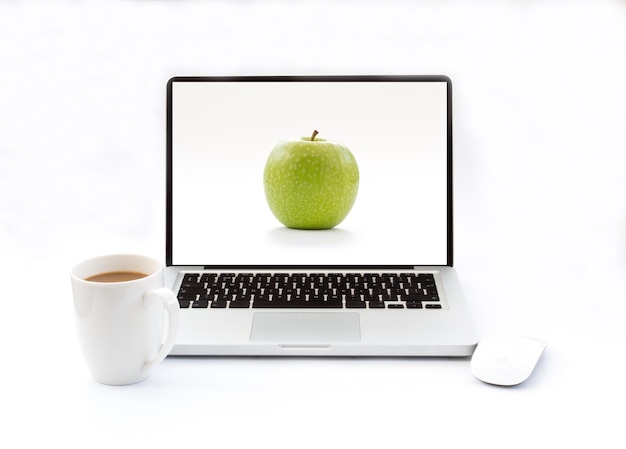 Laptop with apple on screen in front of coffee cup against white background