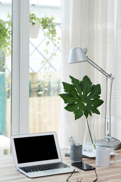 Laptop with black empty screen, cup of coffee and smartphone of table in home office of person