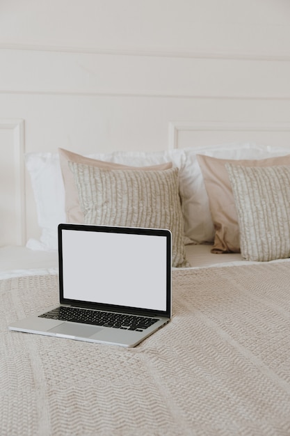 Laptop with blank copy space screen display in bed with plaid, pillows against white wall