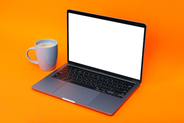 Laptop with blank screen and cup of coffee on orange background