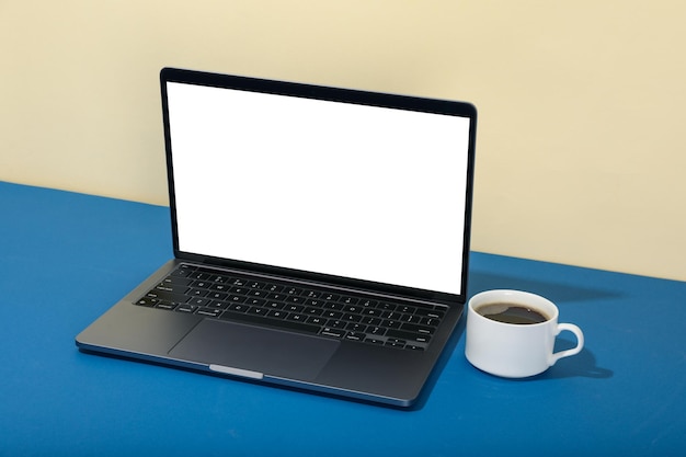 Laptop with blank screen and cup of coffee on two tone background