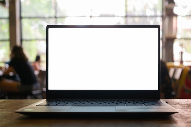 ぼやけているコーヒーショップの背景を持つテーブルに空白の画面を持つノートパソコン。