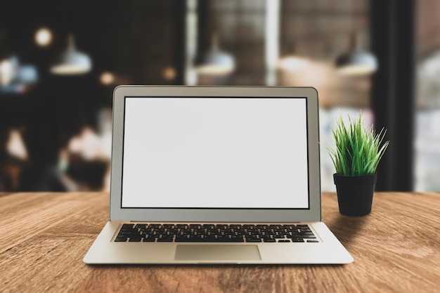 Laptop with blank screen on top of wood table with tree at coworking space