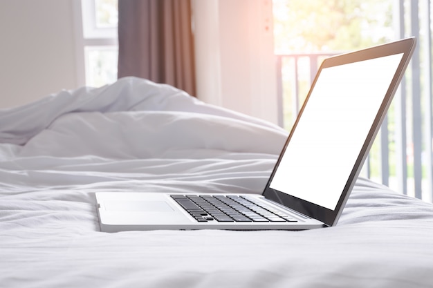 Laptop with blank screen on white bed in morning