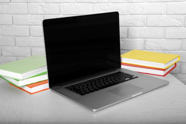 Laptop with books on brick wall background