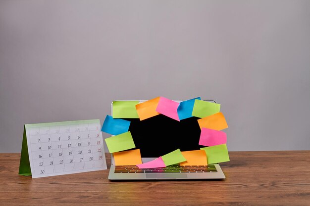 검은색 화면이 열려 있는 나무 책상 노트북 PC에 다채로운 스티커 메모와 달력이 있는 노트북