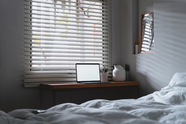 Computer portatile con schermo vuoto spazio copia e letto con lenzuola bianche