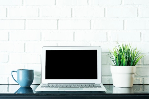 Laptop with empty space on screen with coffee cup and green plant pot on table