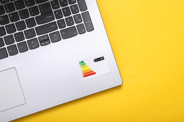 Laptop with graph class of energy consumption on yellow background Top view