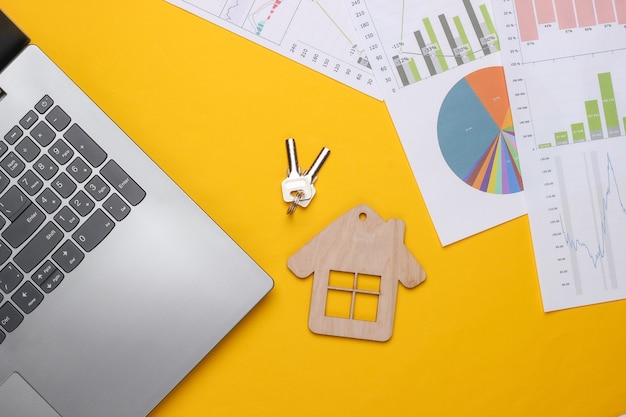 Фото Ноутбук с графиками и диаграммами, фигура дома на желтом фоне. бизнес-план, финансовая аналитика, статистика. вид сверху