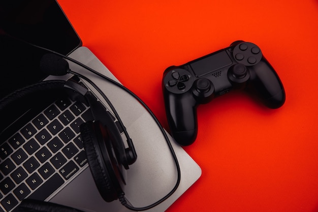 Laptop with headphones, gamepad on red background.