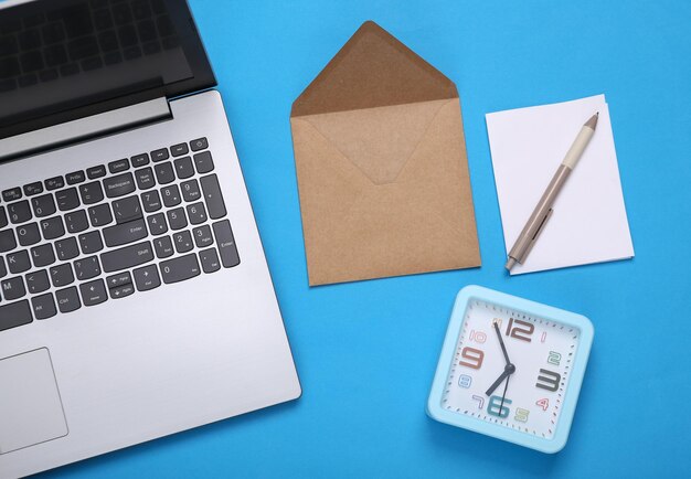 Laptop with letter alarm clock on blue background Email Flat lay