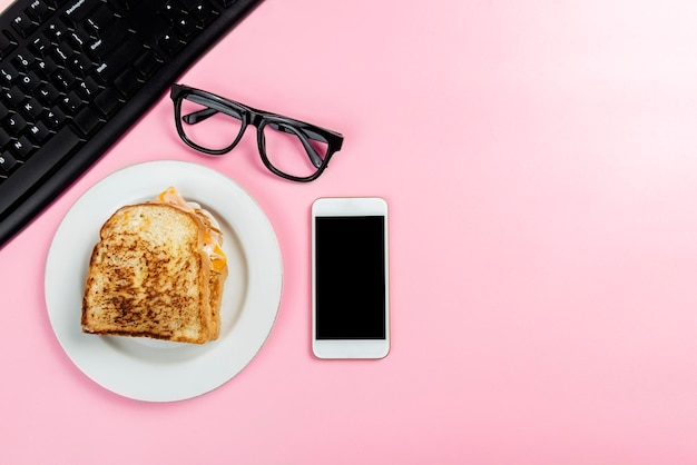 Laptop with mobile phone and bread toast on the plate with colored background