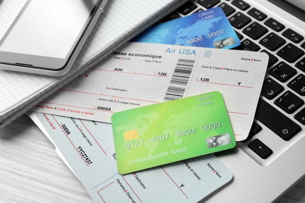 laptop with mobile phone credit cards and flight tickets on light wooden table