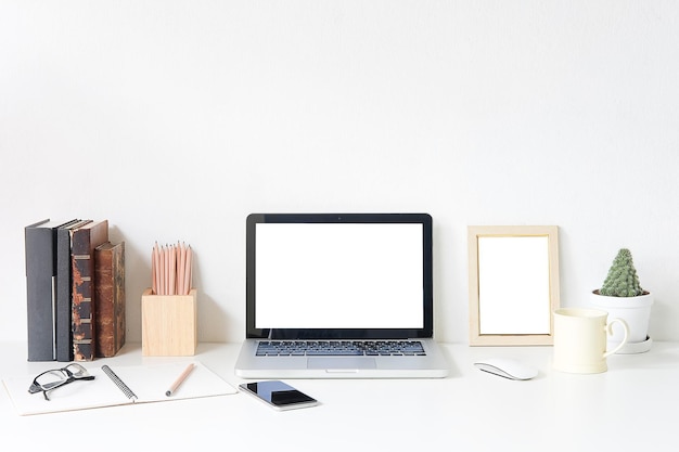 Laptop with office supplies and coffee on desk against white wall at office