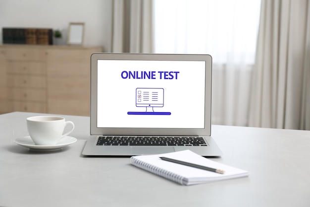 Laptop with online test notebook and cup of coffee on table at home