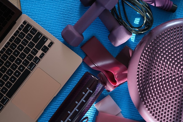 Computer portatile con attrezzatura sportiva viola sulla vista dall'alto del tappetino sportivo