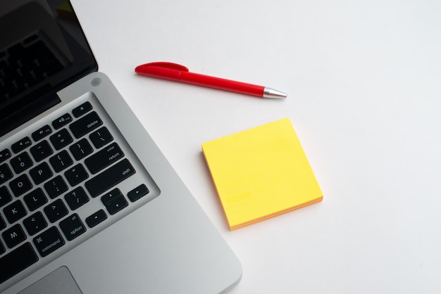 Laptop with red pen and yellow notepads on the desk