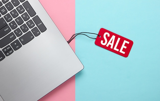 Laptop with a red sale tag on pink blue pastel. Big Sale, discounts, online shopping.