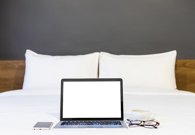 Laptop with a smartphone, coffee cup, and glasses on the bed