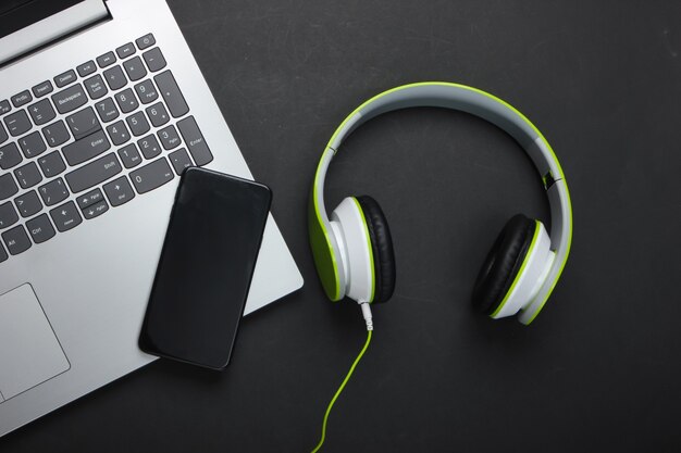 Laptop with stereo headphones and smartphone on black surface