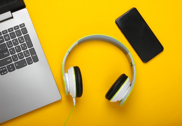 Laptop with stereo headphones and smartphone on yellow surface