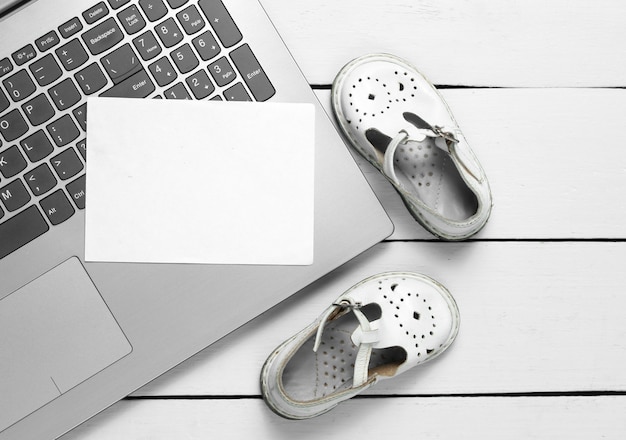 Laptop with white piece of paper for copy space and kids sandals on wooden