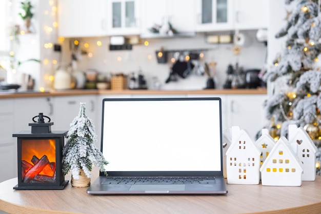 Laptop with a white screen mock up in the cozy white decorated Christmas kitchen with fairy lights