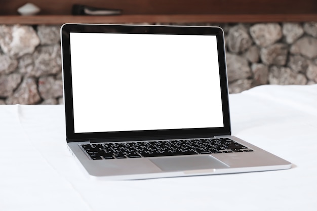 Laptop with white screen mockup on white bed.