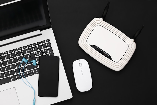 Photo laptop with wi-fi router, smartphone and earphones on black background. studio shot. top view. flat lay