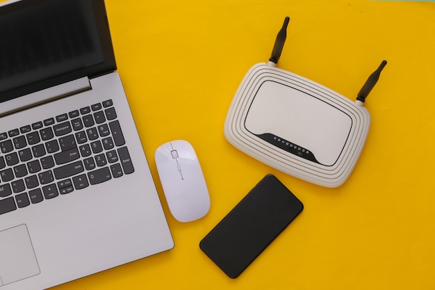 Laptop with wi-fi router, smartphone on yellow background. Studio shot. Top view. Flat lay