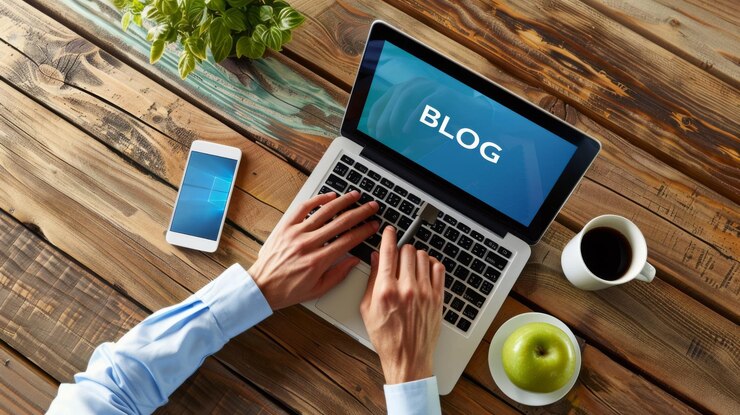 画面にBLOGという単語が書かれたラップトップが,書類や植物に囲まれた机の上に置かれています