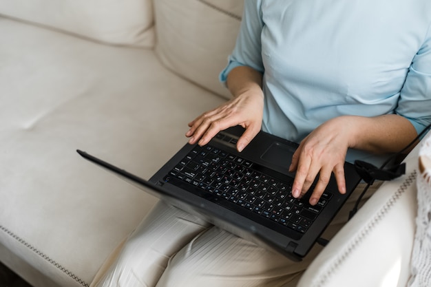 Foto laptop zwart zit op schoot van een vrouw en ze typt met haar handen op het toetsenbord