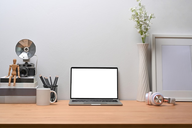 laptopcomputer, fotolijst, boeken, potloodhouder en koptelefoon op houten bureau.