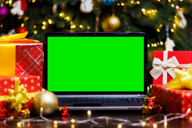 Laptopcomputer met groen leeg scherm op tafel met geschenken en een krans