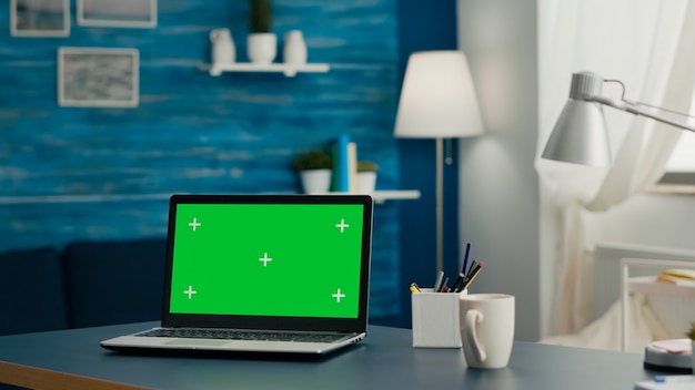 Laptopcomputer met mock-up groen scherm chroma key-display staande op tafel in de woonkamer. Pc met geïsoleerd scherm in thuiskantoorstudio met niemand erin