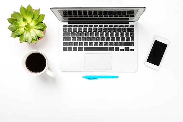 Laptopcomputer met plant in een pot, kopje koffie, moderne mobiele telefoon en blauwe pen op witte achtergrond.