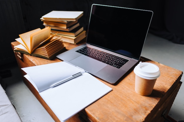 Laptopcomputer op de houten tafel met boeken, notitieboekje en kopje koffie in de ochtend.