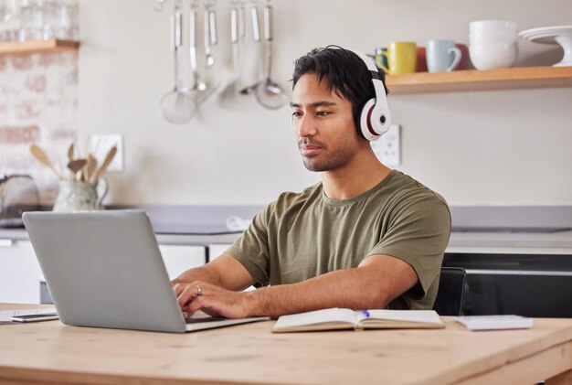 Foto laptopkeuken en student met muziekkoptelefoon om naar rocknummer te luisteren terwijl ze aan onderzoeksproject werken. jonge gen z-man ontspant thuis terwijl hij audiopodcast of radio streamt voor rust en welzijn